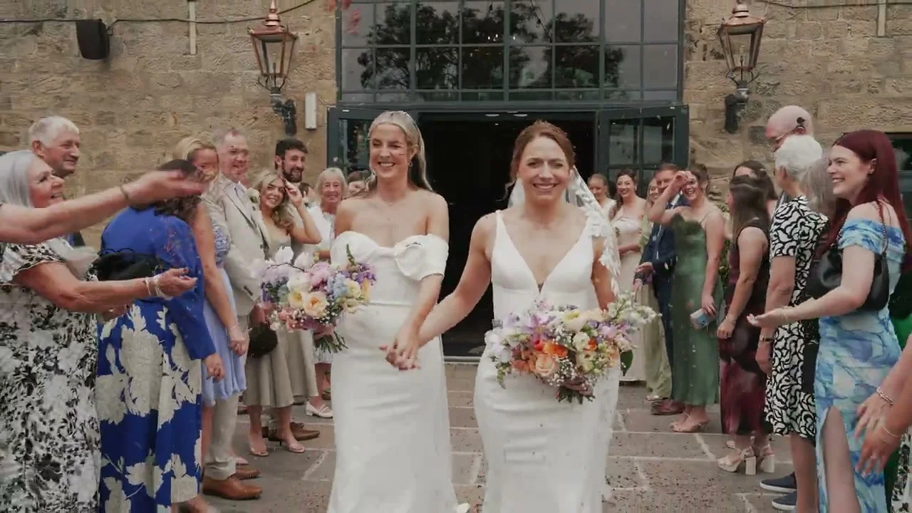 Amy and Louise walking through confetti with their wedding guests